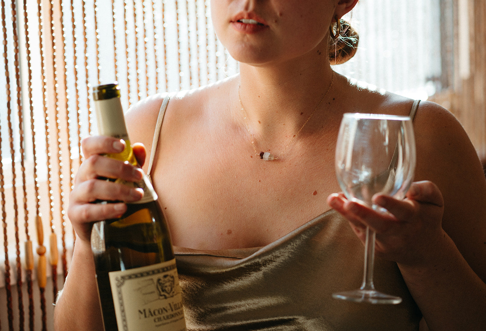 a woman wearing gold birthstone jewelry and holding a bottle of champagne